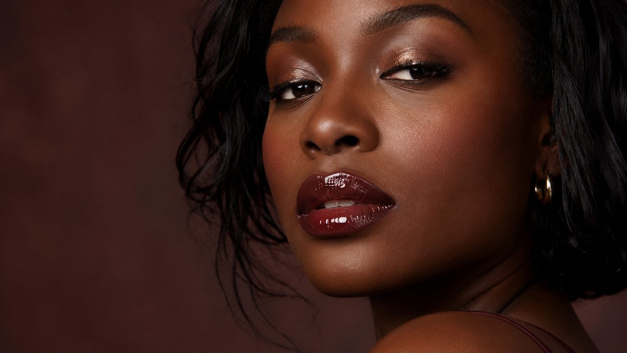 Woman with rich dark complexion wearing a glossy burgundy lip shade